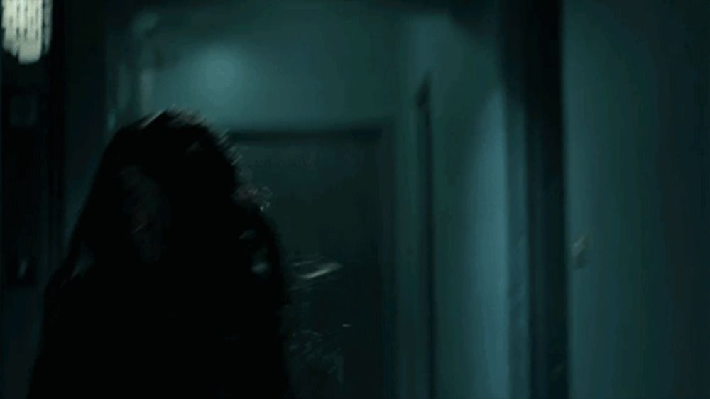 a woman in a leather jacket is running through a dark hallway in a dark room .