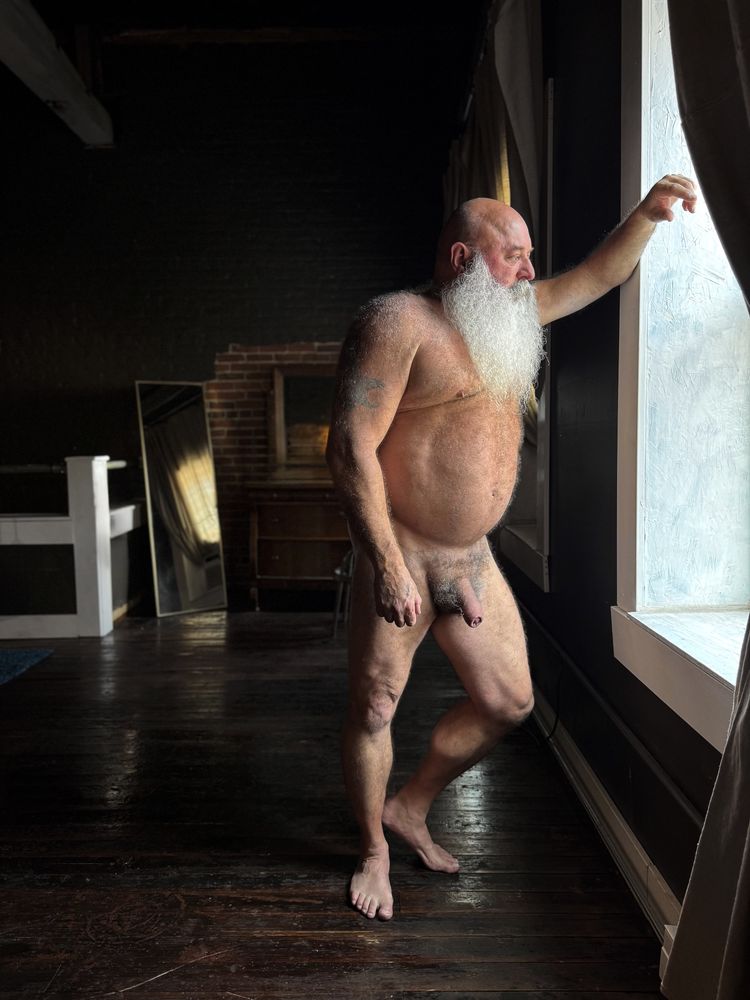 Nude male, 50's, standing in window of a warehouse loft, natural light, shallow depth of field. 