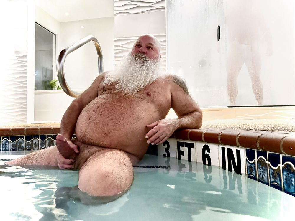 Nude, aroused, older male with large white beard, reclining at a pool's edge