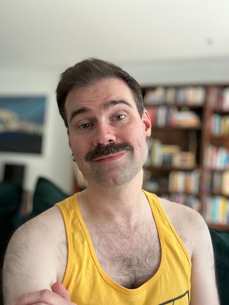 a photo of me wearing a yellow tank. a blurred bookshelf and painting is in the background.
