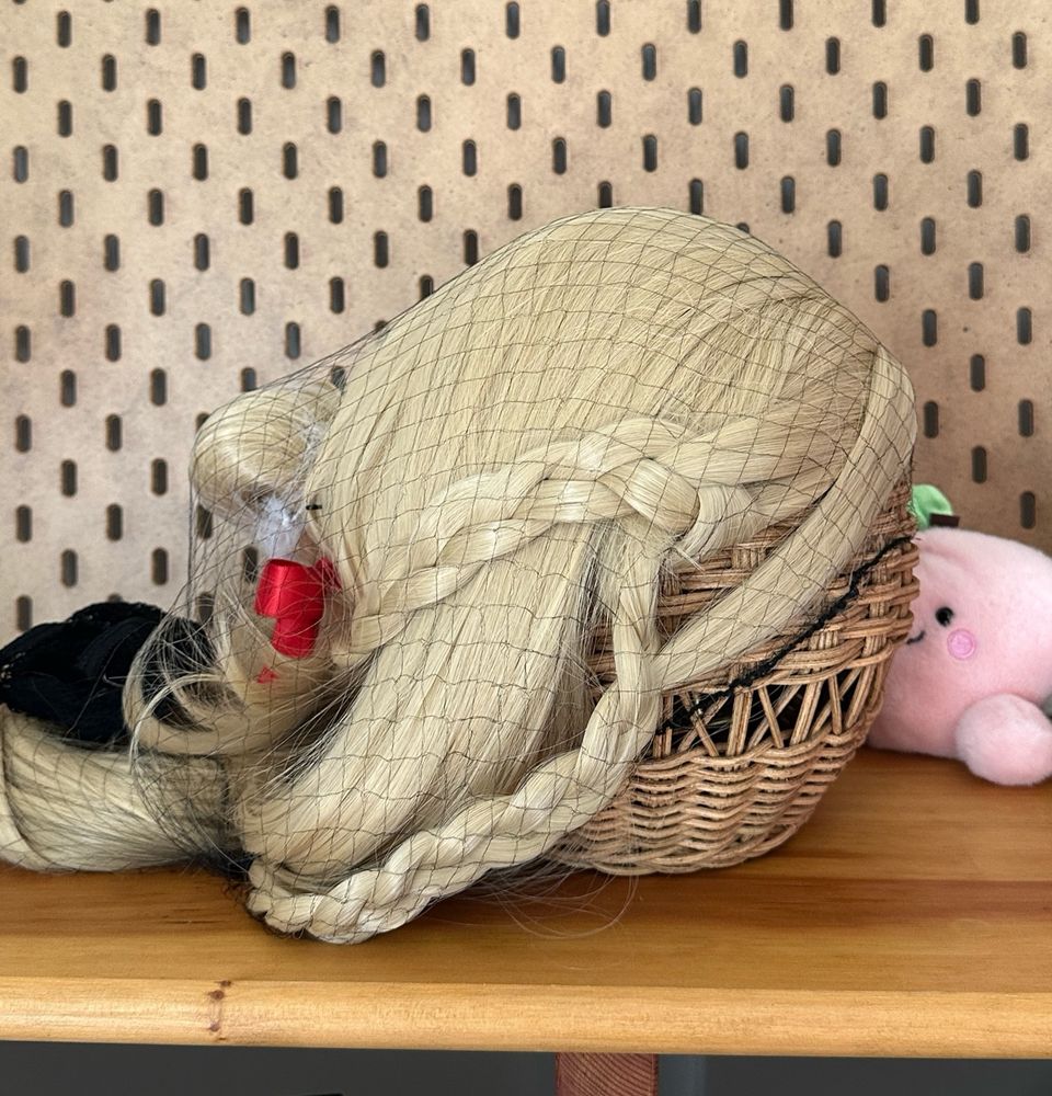 A blonde wig in a wig net on a desk in front of a pegboard.