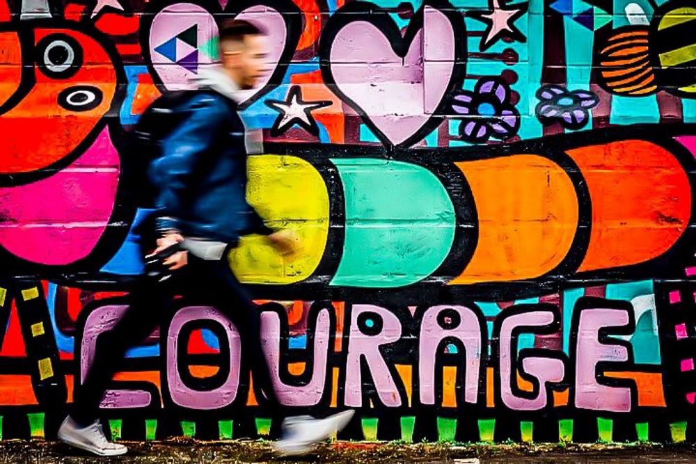 Graffiti. Eine bunte Raupe auf vielfarbigem Hintergrund mit rosa Herzen.
Schriftzug: COURAGE (französisch für Mut)
Ein junger Mann zielstrebig daran vorbei. So schnell, das seine Konturen verschwimmen
