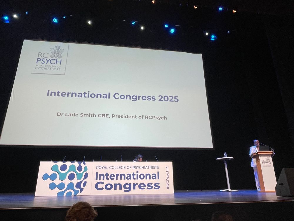 Dr Lade Smith, President of Royal College of Psychiatrists giving welcome address at RCPsych International Congress 2025. Standing on stage behind podium next to giant slide.