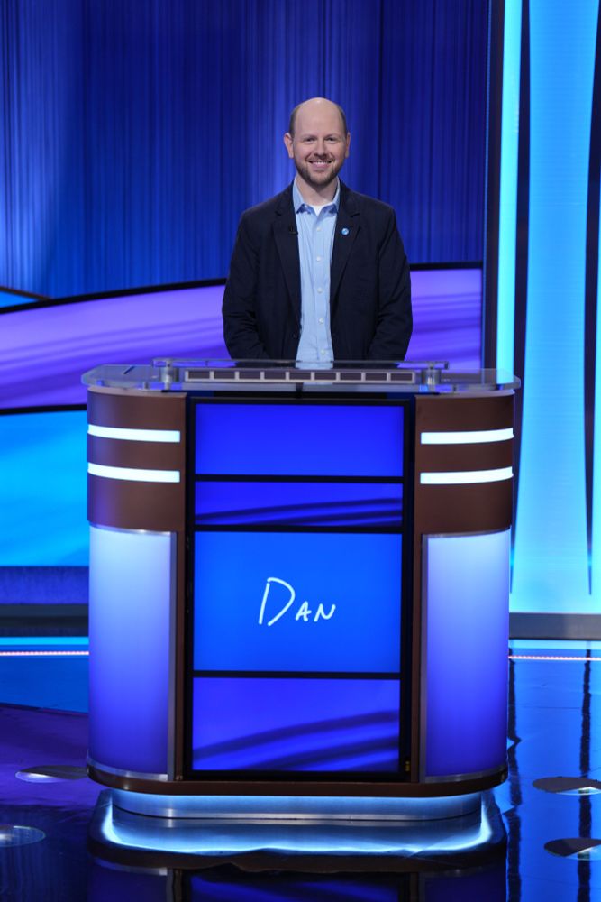 Dan standing behind a Jeopardy! contestant podium. 