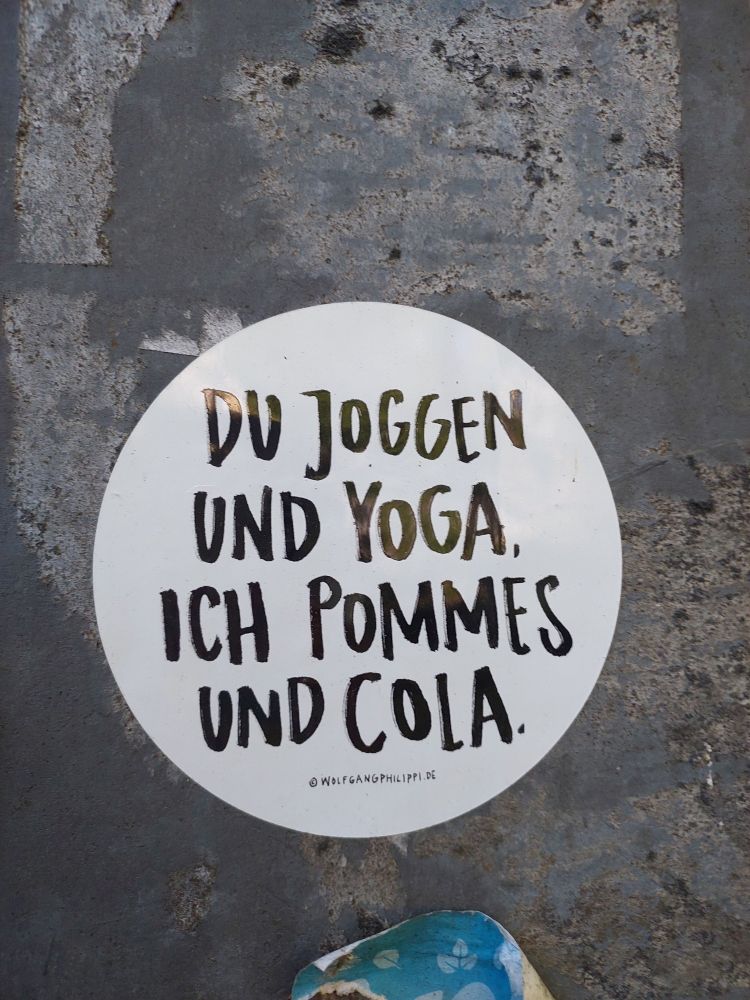 Ein Aufkleber mit dem Text: "Du Joggen und Yoga. Ich Pommes und Cola."
