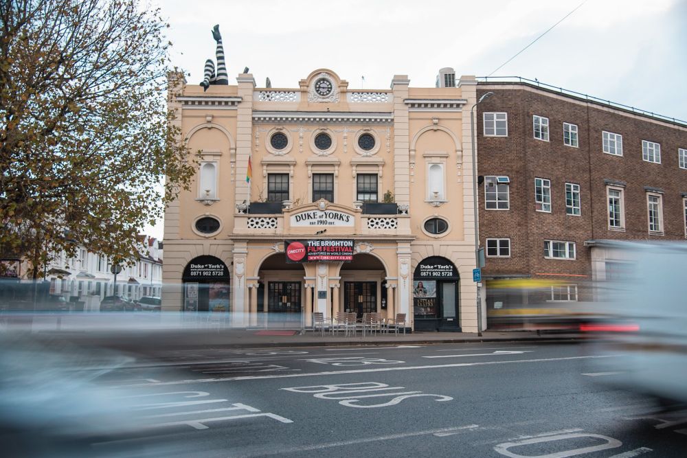A long exposure photograph of the Duke of Yorks picture house, the venue for FFConf. There are light trails from cars that are passing by in front of the building.