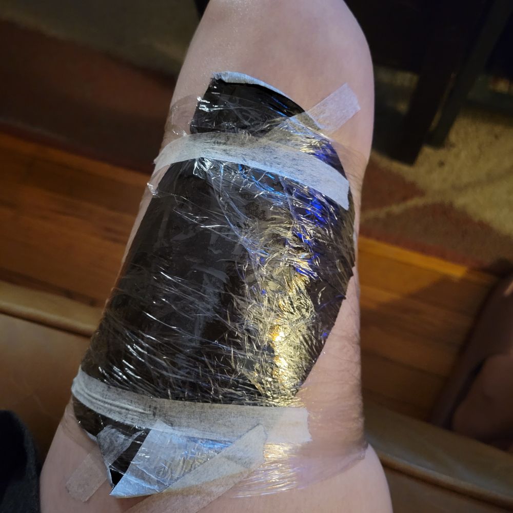 A black bandage covering a new thigh tattoo. The bandage is wrapped in plastic wrap to keep it in place.