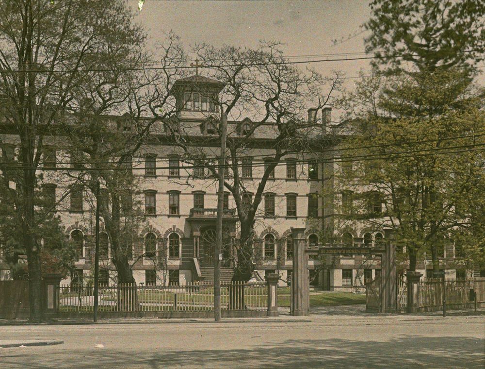Photo of a large Victorian four-story school building, with a yard and trees.