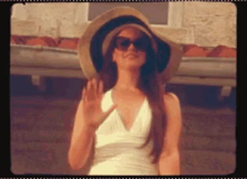 a woman wearing a hat and sunglasses is waving at the camera .