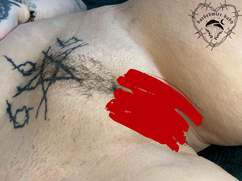 close up of Bug’s pussy, censored with a red scribble, but their tattoo and landing strip are visible. Their legs are parted only slightly. 