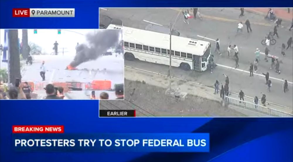 Broadcast news screengrab showing protesters surrounding a white bus and also impromptu shopping cart barricade with fire in the street 