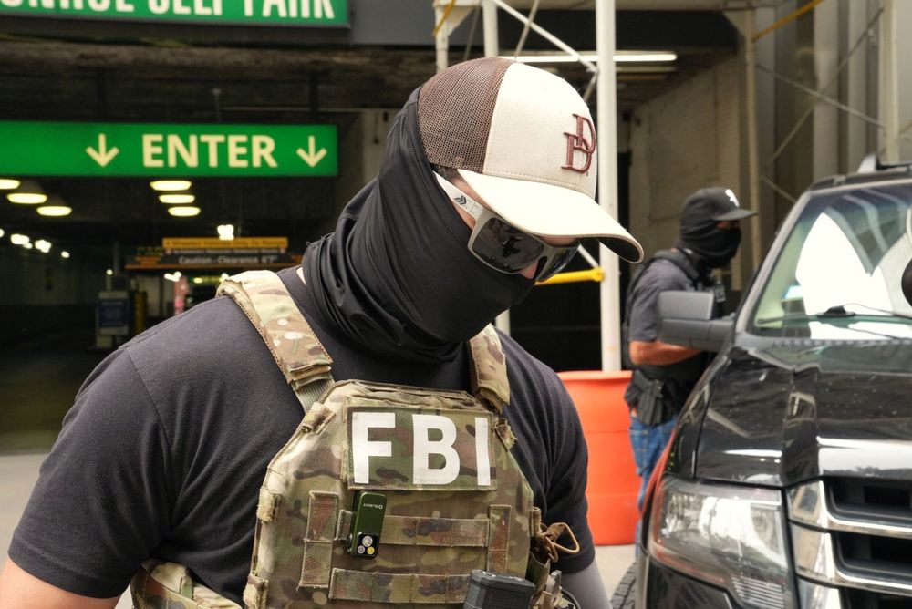 FBI agent with black face gaiter sunglasses ball cap 