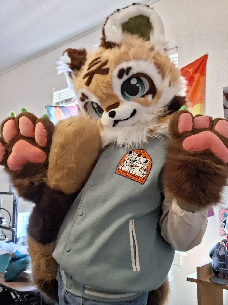 Jade with both paws up showing of a "queer animal club" patch