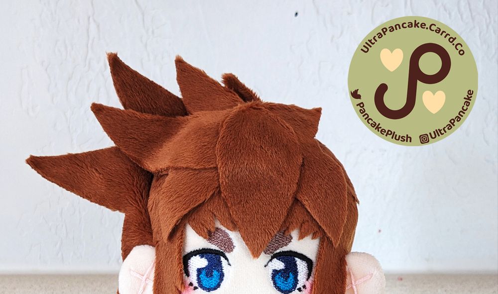 Some bright blue embroidered eyes are peeking just into frame of the picture. The top of a mystery plush's head is visible with just the eyes and spiky brown hair to identify it. Who could it be?