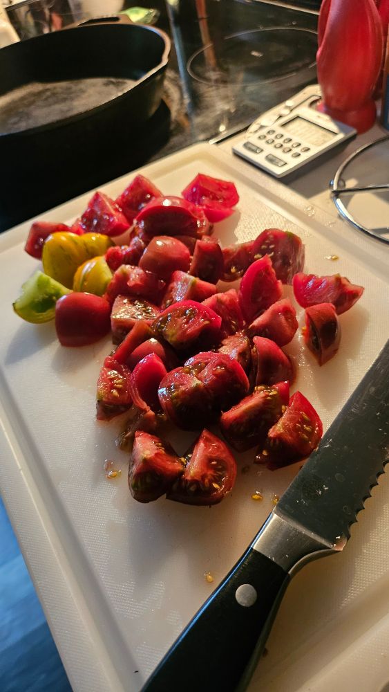 gorgeous quartered plum tomatoes on a cutting board with a serrated knife