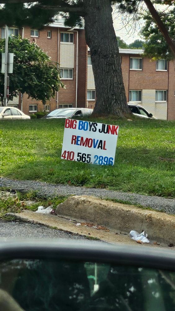 a homemade sign stuck in a lawn that says BIG BOYS JUNK REMOVAL 410.565.2896