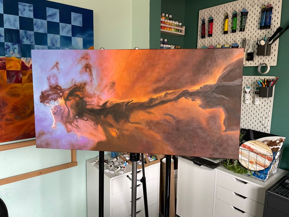 10x30” canvas on easel of a nebula in progress. The left is lavender and light blue fading into pink, orange, then brown. There is a spire that runs across the center of the piece in the same colors. 
