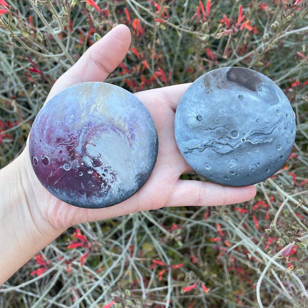 Two small round clay disks in my hand painted with acrylics to look like Pluto and Charon.