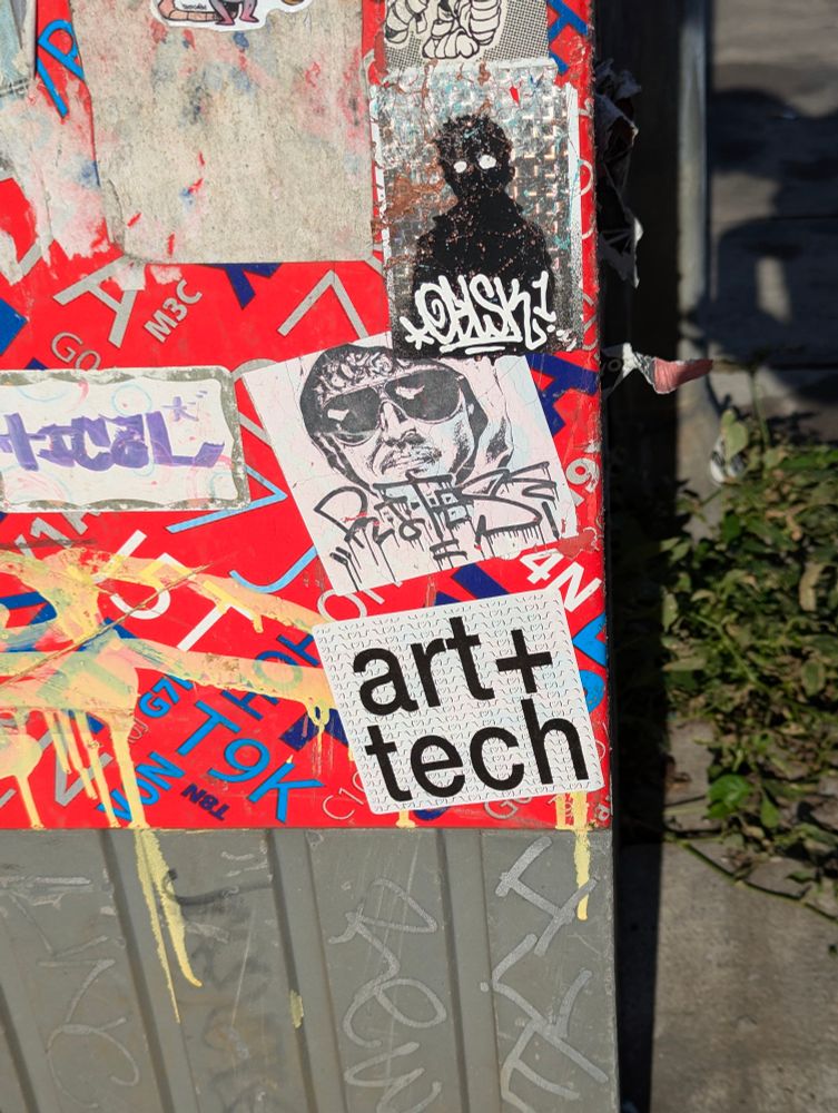 A sticker on a utility pole reading ART + TECH 