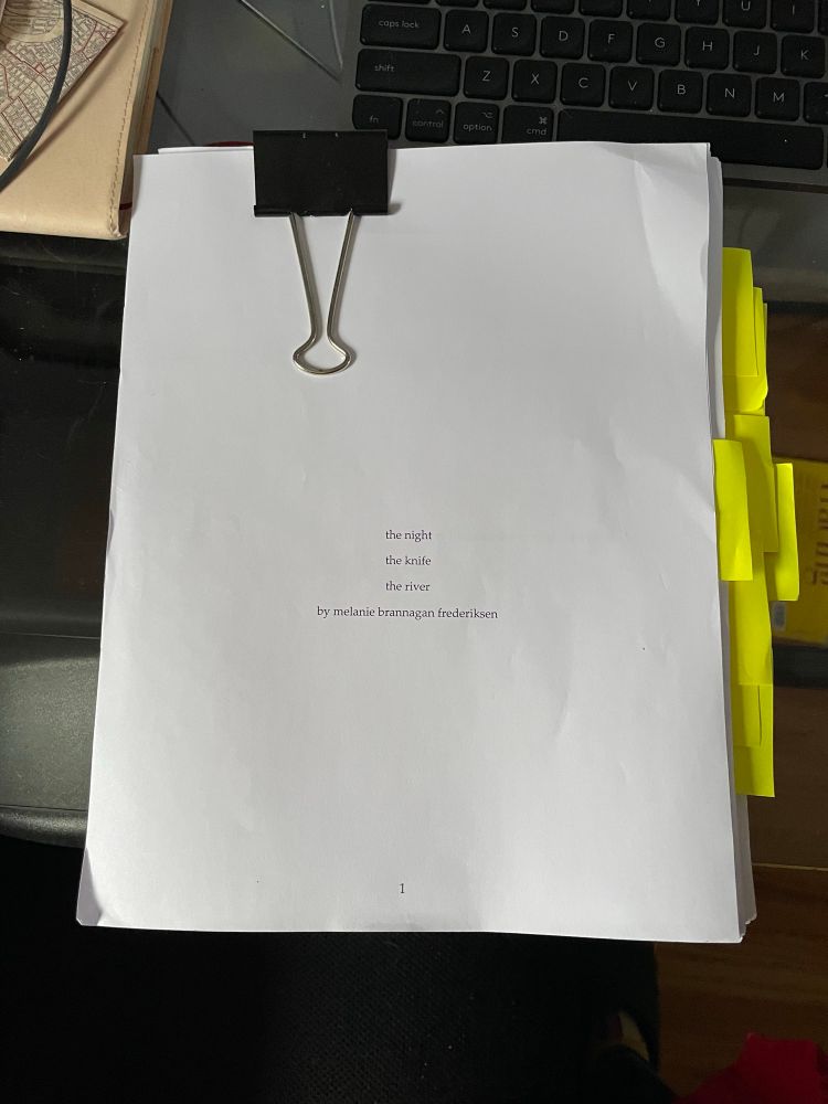 a manuscript print-out flagged with a number of fluorescent yellow post-it notes on a glass-top desk