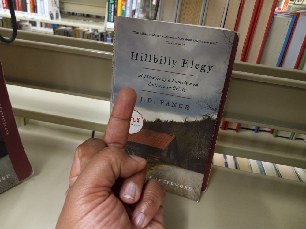 A black woman's hand flipping off a copy of J.D. Vance's Hillbilly Elegy
