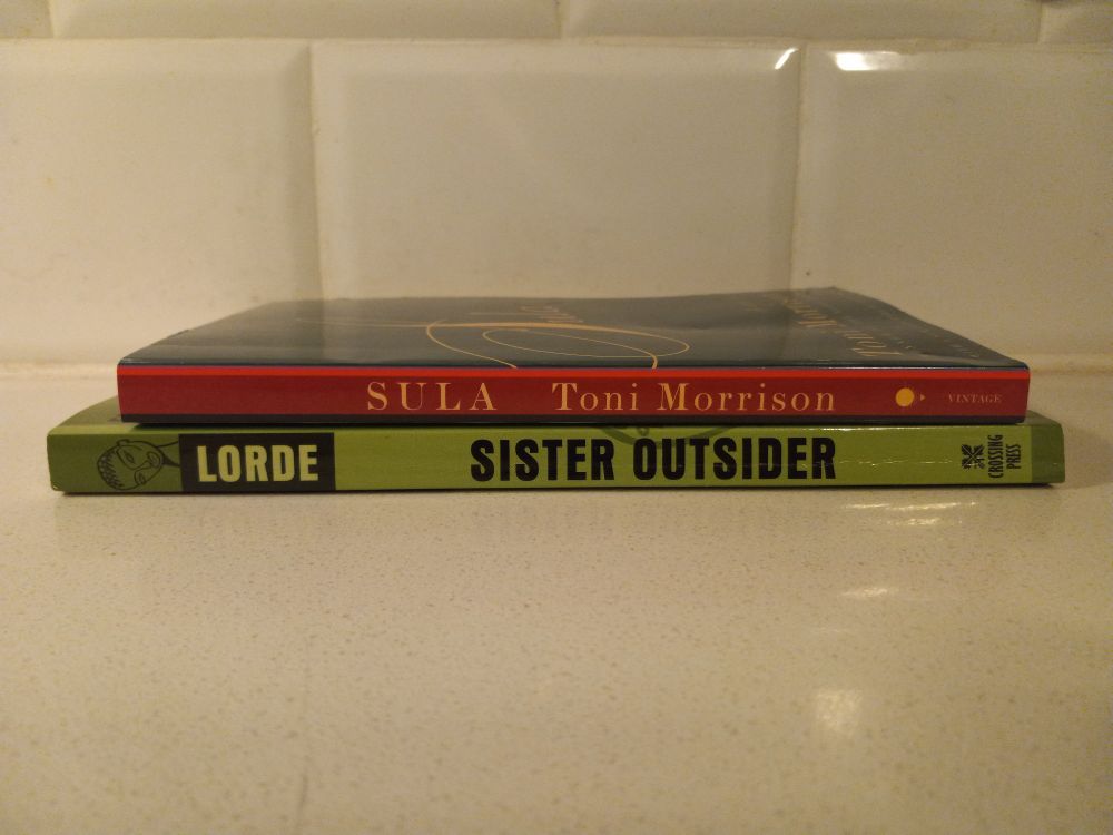 Copies of Toni Morrison's Sula and Audre Lorde's Sister Outsider stacked on top of each other on a white kitchen counter. 