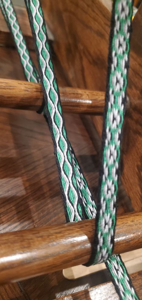 Close up of a narrow green woven band on an inkle loom.
