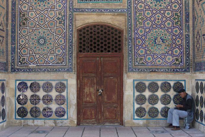 old man sitting in the heat in front of a pretty building in Kazakhstan