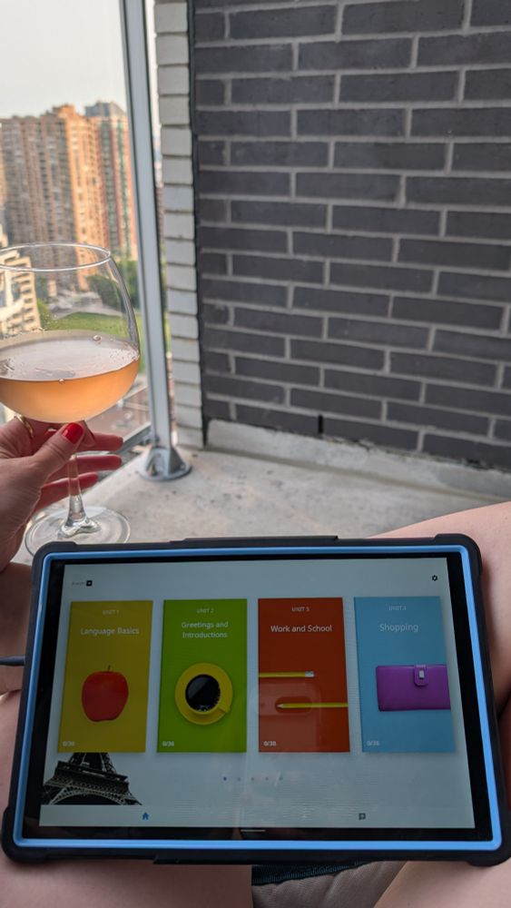 A balcony with me holding a glass of wine and Rosetta Stone lesson selector screen on an inexpensive tablet in a black and blue case