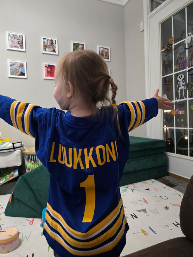 a young girl facing away from a camera to show the back of a blue and yellow hockey jersey with the name Luukkonen and number 1 on the back