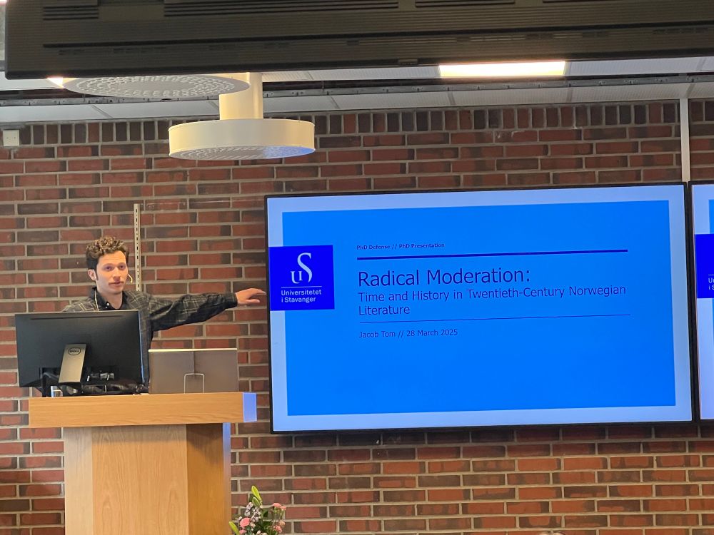 Man at lectern. Screen shows thesis title Radical Moderation