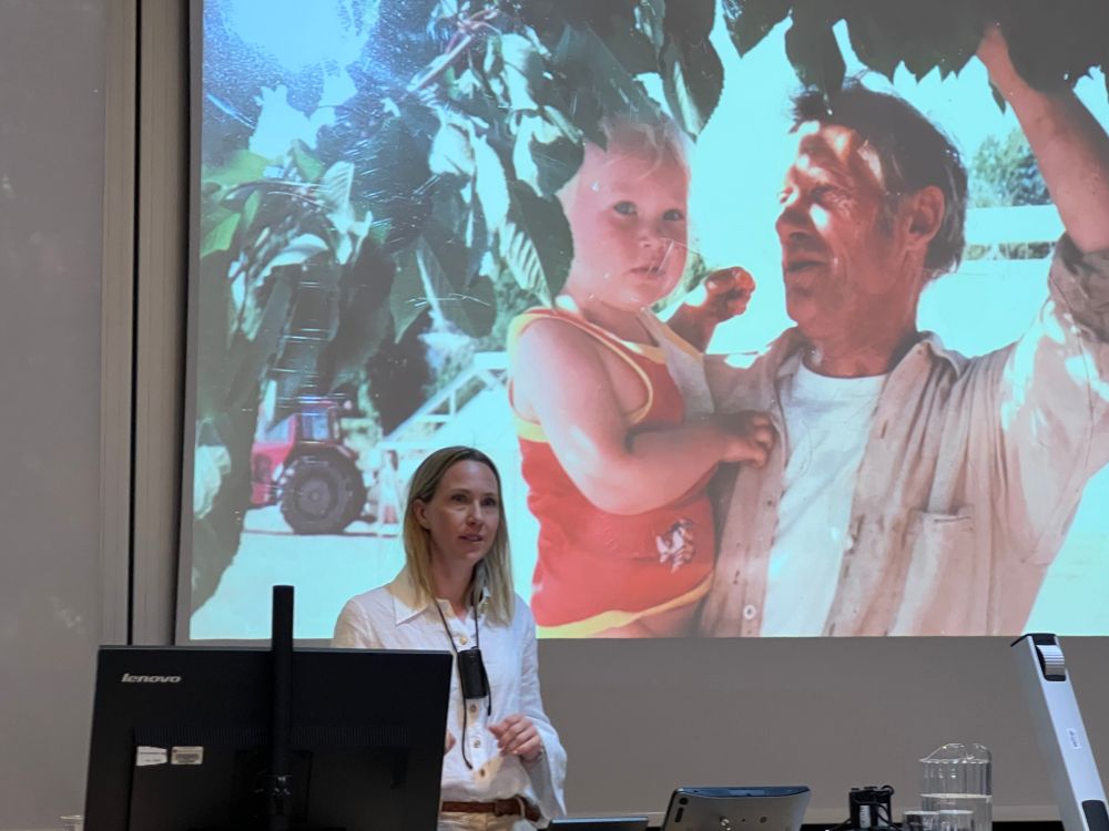 Woman in front of screen with picture of a grandfather holding granddaughter under a tree