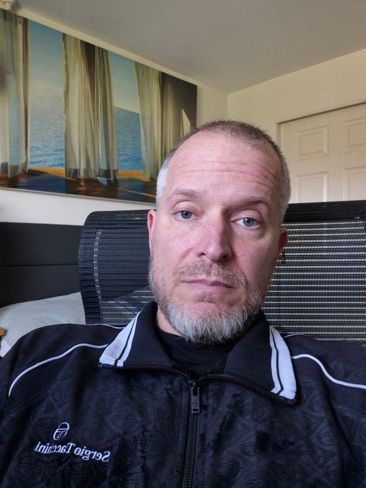 Brian is sitting in his desk chair at home wearing a black valour tracksuit suit