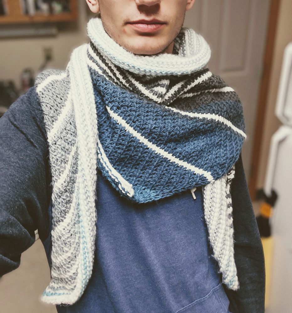 A crocheted scarf. Its colors are white stripes alternating with a blue and gray gradient.