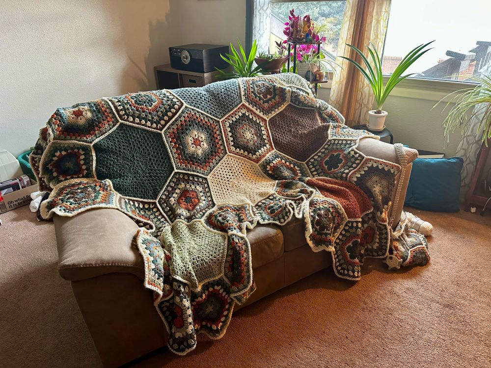 A blanket draped over a love seat. The blanket is made of solid-color heptagonal panels and multi-color hexagonal panels, joined in a regular tiling that causes the angle of each vertex to exceed 360°, giving the blanket a ruffled edge.
