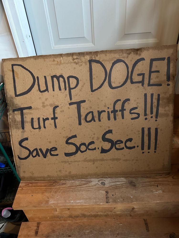 Very soggy signs that says “Dump DOGE!Turf Tariffs!!! Save Soc. Sec.!!!”