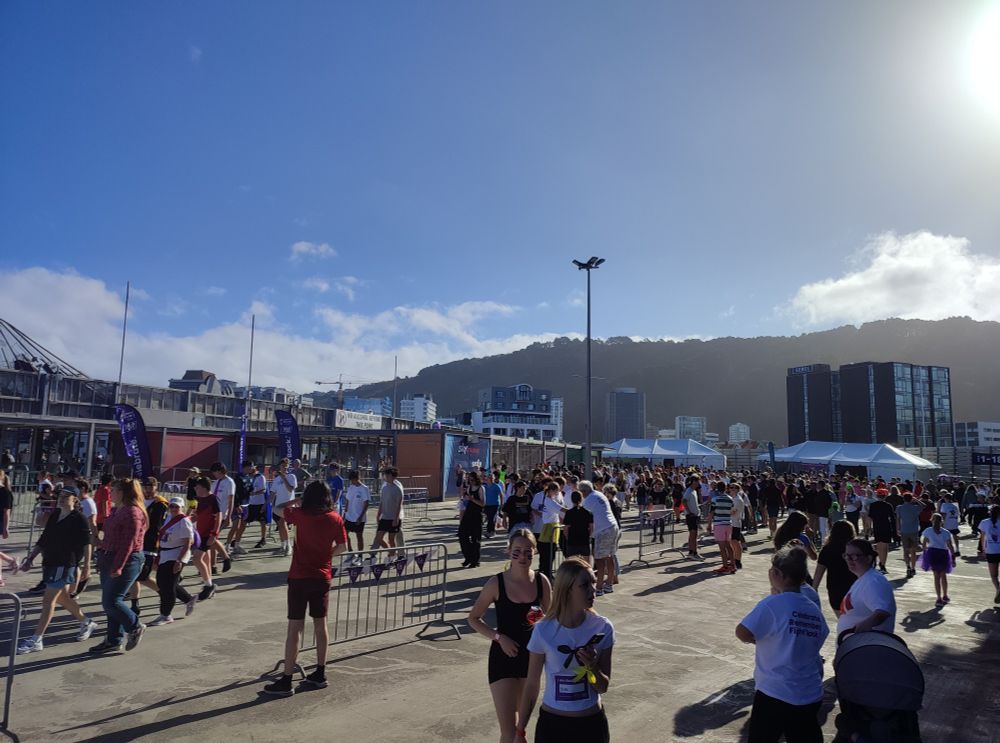 Crowd of people in athletic gear running and walking in golden evening light in a car park surrounded by food trucks and banners