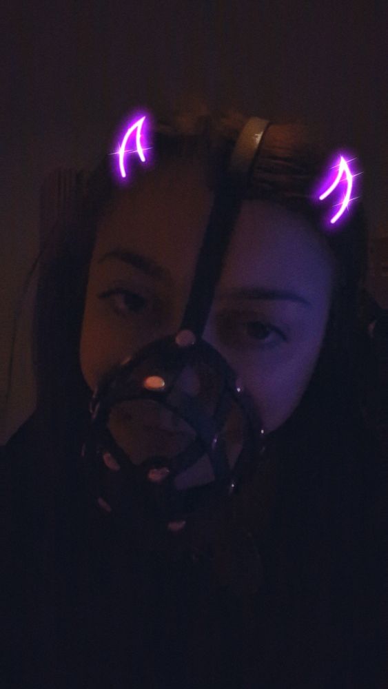 Dani in her muzzle in her dark bedroom. She has purple horns from a snapchat filter