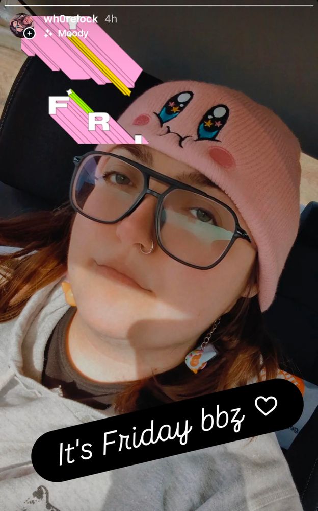 Dani looking moderately grumpy, in her car, with her Kirby hat on and a caption that says "it's Friday bbz <3"