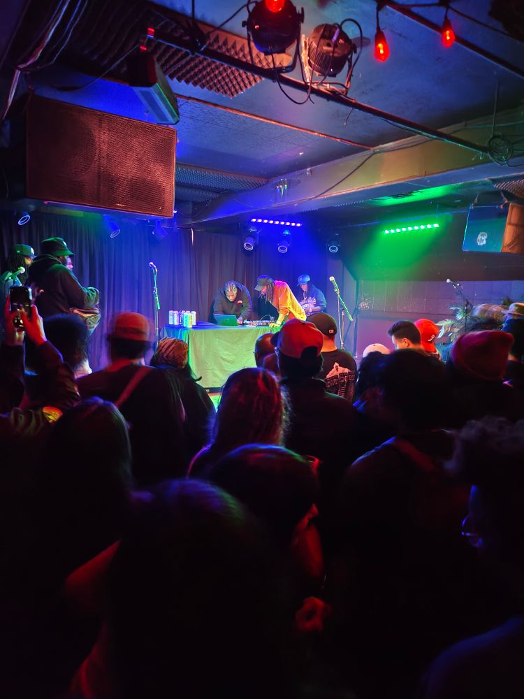 Two men on stage silently lean over a laptop computer while a fully packed venue looks on in anticipation.