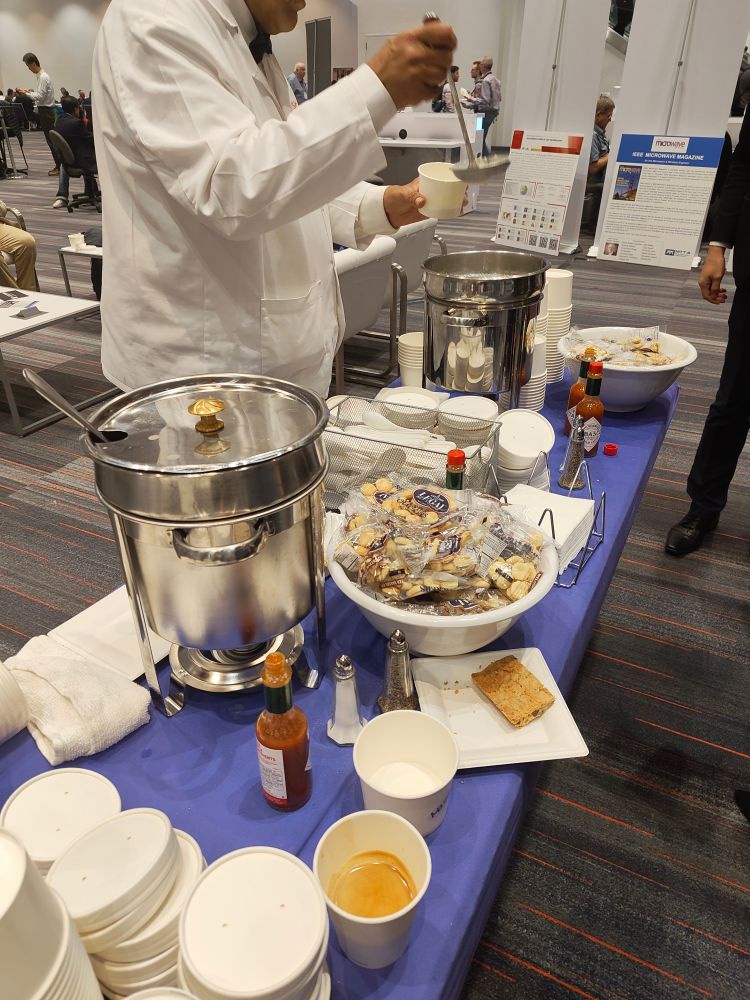 Man in a white chef coat serves clam chowder at a microwave electronics conference.