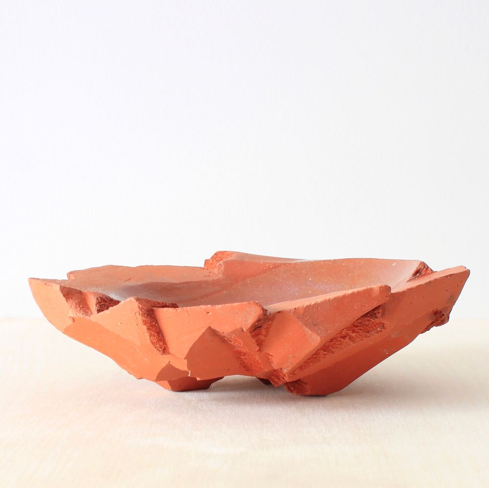 An earthenware serving bowl. It is approximately 14 inches in diameter. The interior volume is glazed with a glossy finish in most areas. Other places the glaze tacitly fades in and out. The interior curve is smooth while the exterior is chunky and blocky reminiscent of a pile of rocks.