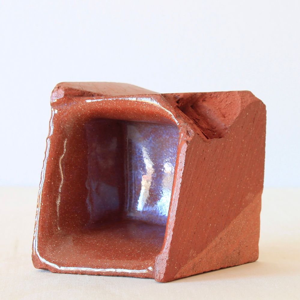Close cropped photo of the interior of the same earthenware cup. It's smooth glaze contrasts with brushed, scraped and jagged parts of its exterior.