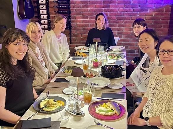 7 women sitting at a dinner table smiling towards the camera: Eline Muijres, Romy Halfweeg, Anna Weber, Marina Diez, Regina Reisinger, Trisha Lee and Jodie Azhar