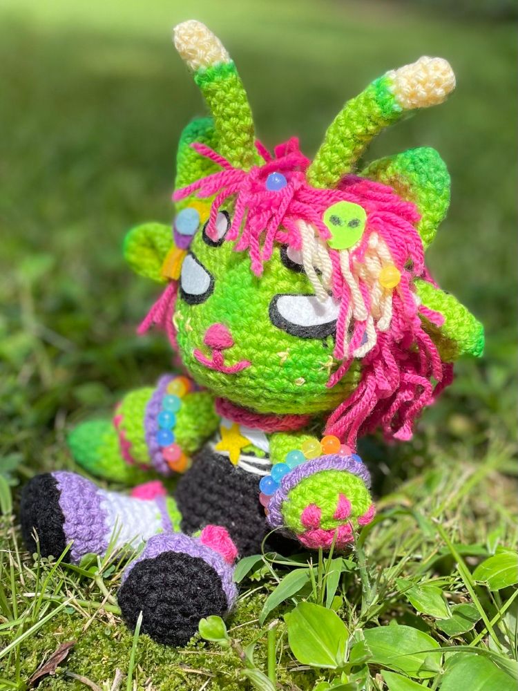 right side view of alien doll, showcasing small beads and a felt alien head decoration in the yarn hair