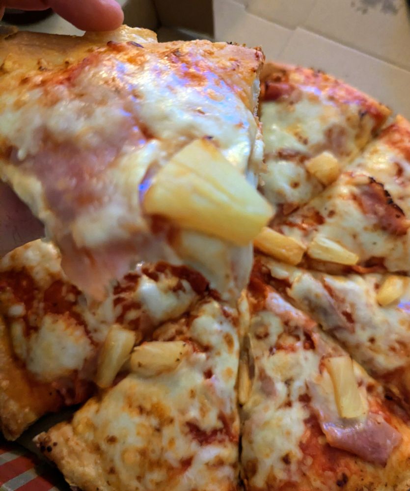 Eine Pizza Hawaii mit extra dickem Boden. Das erste Stück ist angebissen.