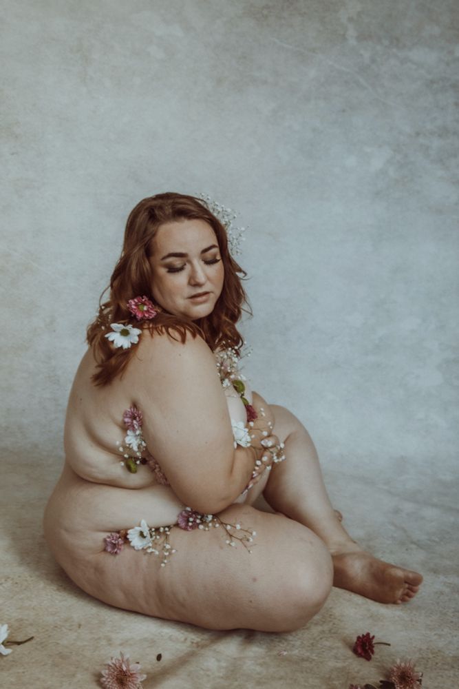 Fat white woman seated with flowers tucked into her body and hair 