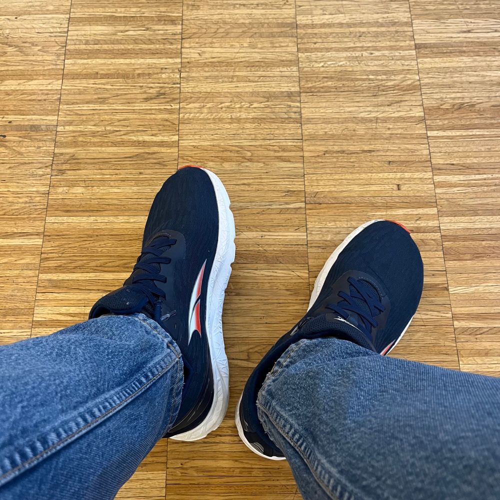 Ein heller Parketfussboden und zwei Füße in blauen Turnschuhen.