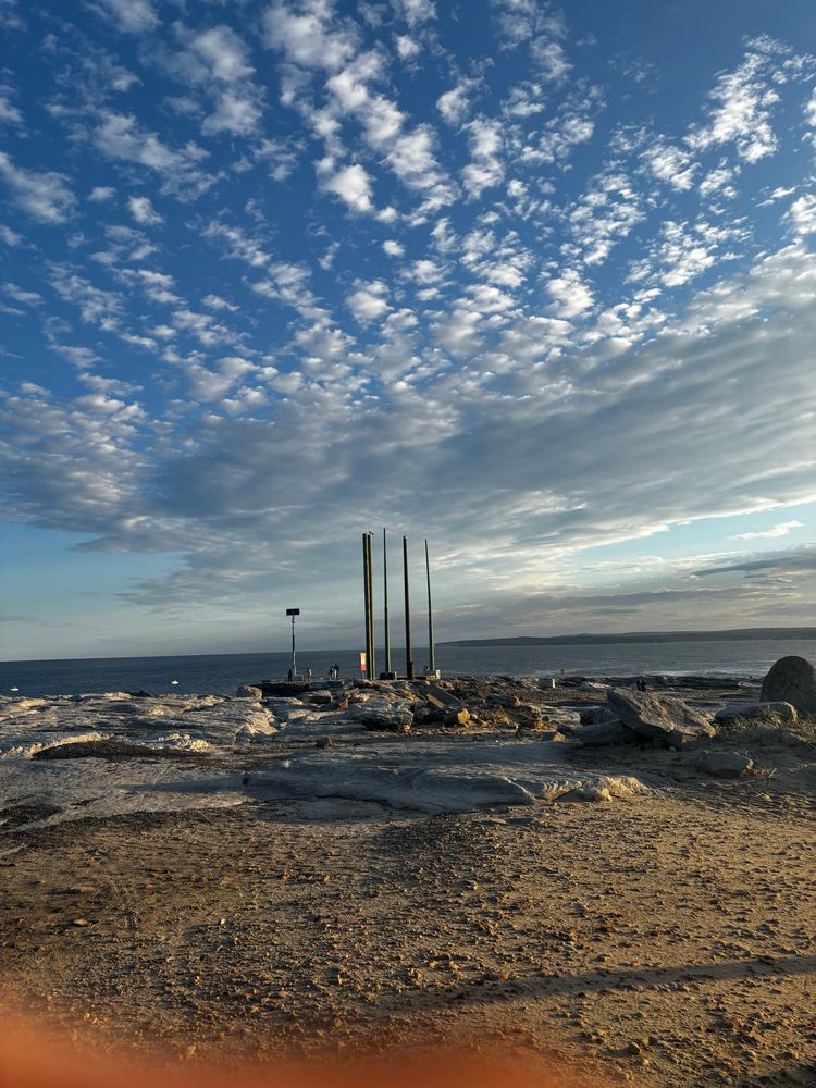 Five pillars at afar on a rocky landscape, in front of the sea and thinly clouded sky 