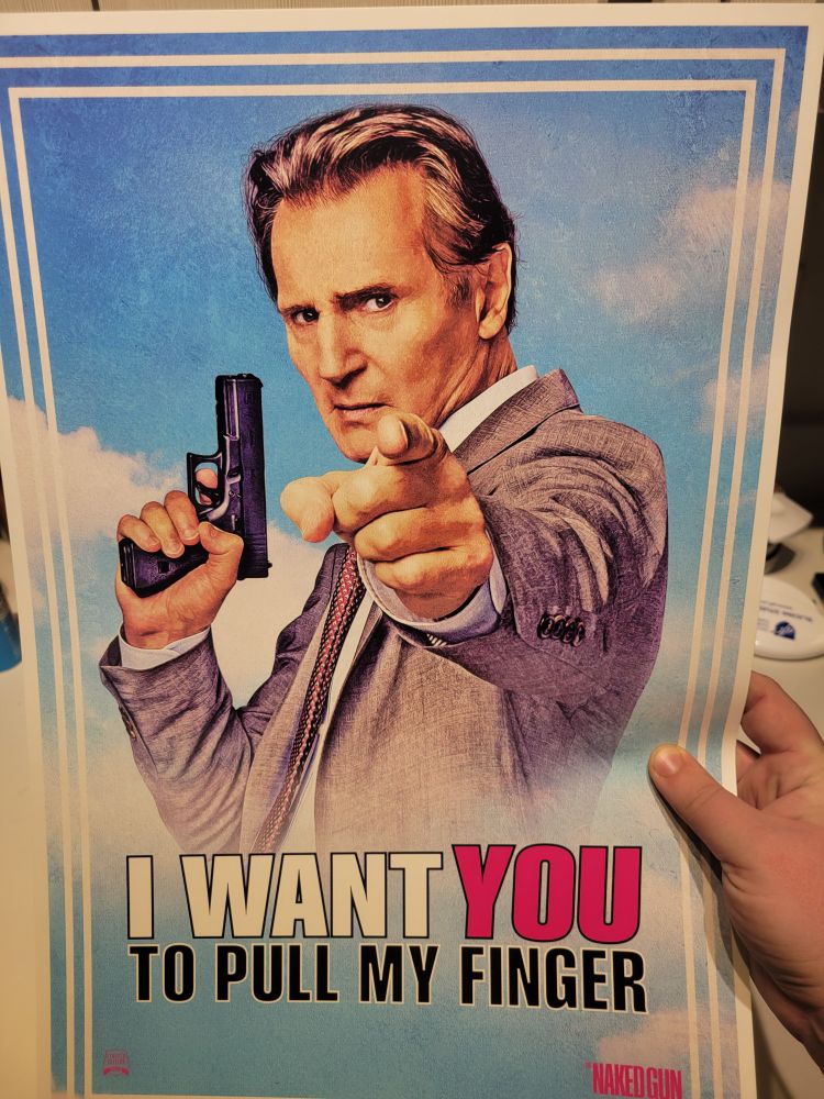 A hand holding a poster for "The Naked Gun" showing Liam Neeson holding a pistol in one hand and pointing his finger at the viewer. The caption reads: "I want YOU to pull my finger." 